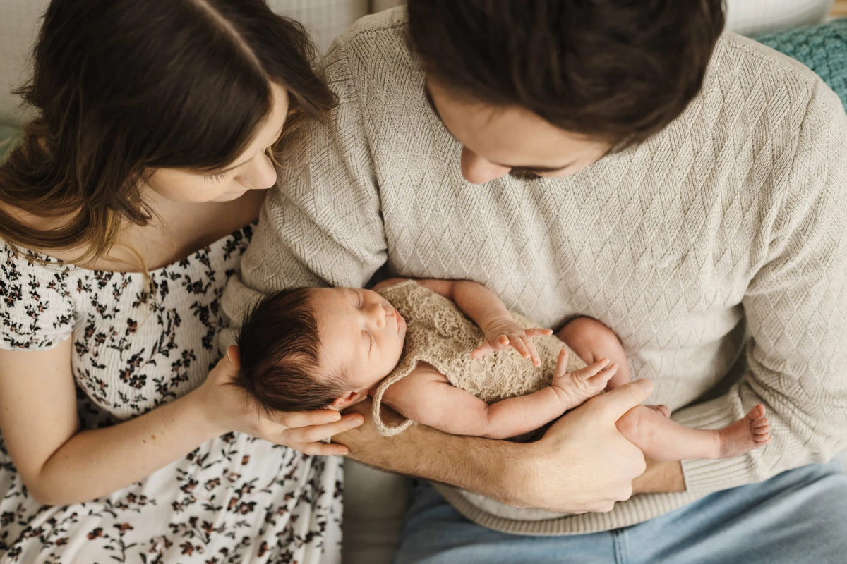 Two parents gazing down at their sleeping newborn, cradled in their arms